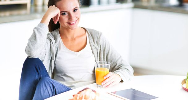 Jonge vrouw met sinaasappelsap en tablet in keuken. - Foto, afbeelding