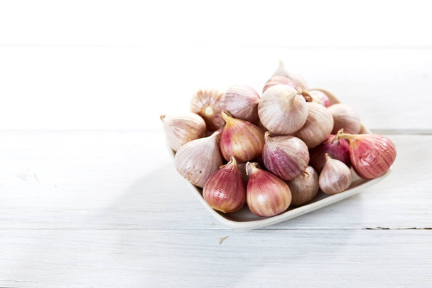 Fresh garlics in ceramic bowl on wooden white table background - Fotó, kép