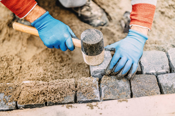 Construction worker placing stone tiles, cobblestone blocks in sand. Portrait of industrial worker - Photo, Image