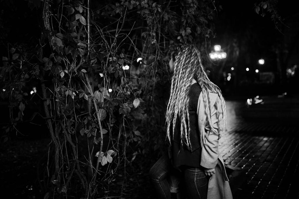 Girl with dreadlocks walking at night street of city against gar - Foto, Imagen