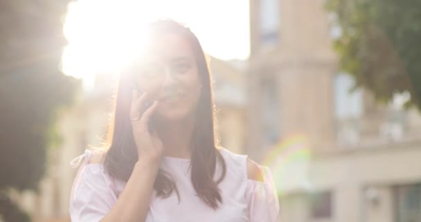 A close up portrait of cute girl chatting on the phone Sun is blurring the photo. Outdoors. - Кадри, відео