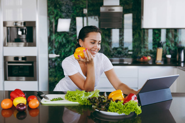 junge Frau schaut sich Rezept in Laptop in Küche an. gesunde Ernährung - Gemüsesalat. Diätkonzept. Gesunder Lebensstil. Kochen zu Hause. Essen zubereiten. mit Platz für Text. - Foto, Bild