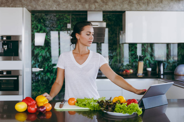 Młoda kobieta ogląda przepis w laptopie w kuchni. Zdrowa żywność - Sałatka warzywna. Pojęcie diety. Zdrowy styl życia. Gotowanie w domu. Przygotowanie żywności. Z miejscem na tekst. - Zdjęcie, obraz