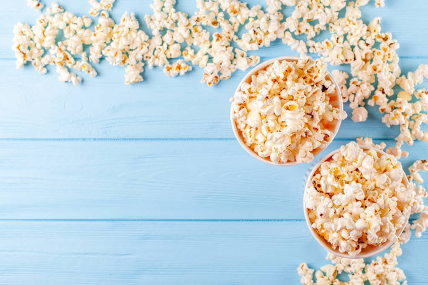 Popcorn horizontal banner. Red stripped paper cup and kernels lying on blue wooden background. Copy space. Top view. - Photo, image