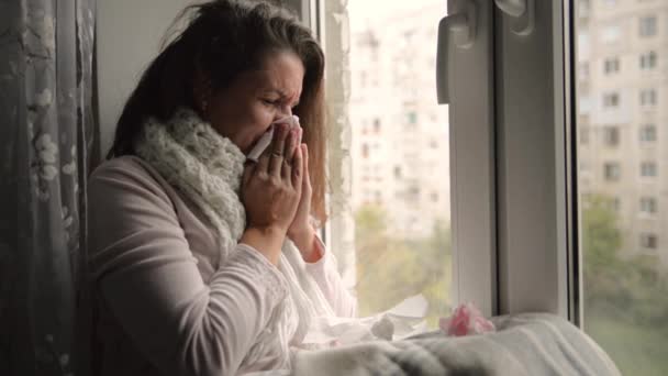 Studená, chlazené žena kýchne. Dívka foukání nosem zatímco sedí u okna. - Záběry, video