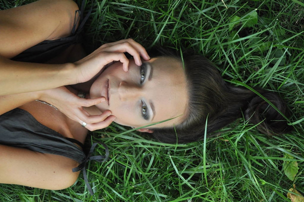 Young woman lying on grass a garden outdoor portrait. Close up portrait of young  girl woman with dark hair.View from above top overhead. Concept of spring summer youth happiness - Photo, Image