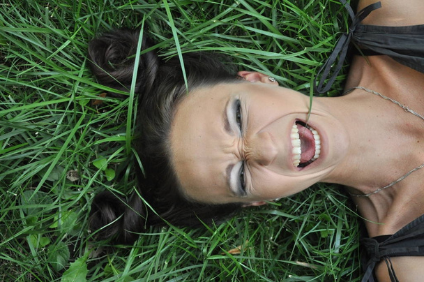 Jonge vrouw liggen op gras een tuin buiten portret. Close-up portret van jong meisje vrouw met donker haar. Bekijk above top overhead. Concept van lente zomer jeugd geluk - Foto, afbeelding