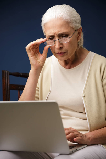 Serious old woman using laptop computer. Looking aside. - Photo, Image