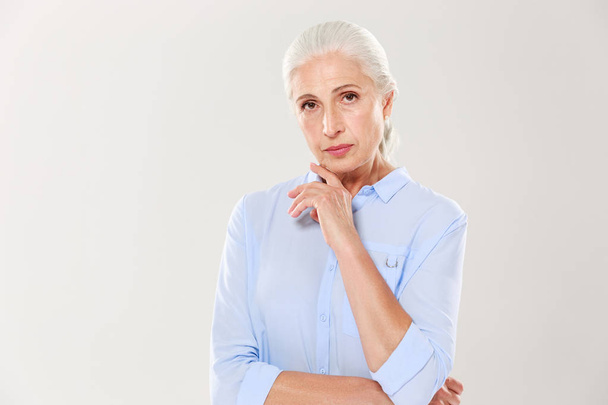 Portrait of charming serious old lady, in blue shirt, touching h - Foto, afbeelding