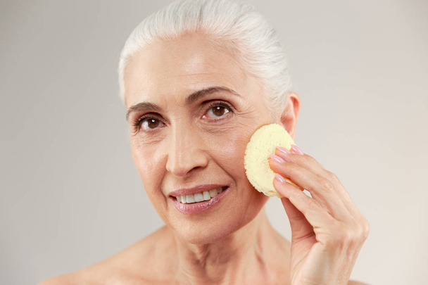 Beauty portrait of a smiling half naked elderly woman using make - Fotó, kép