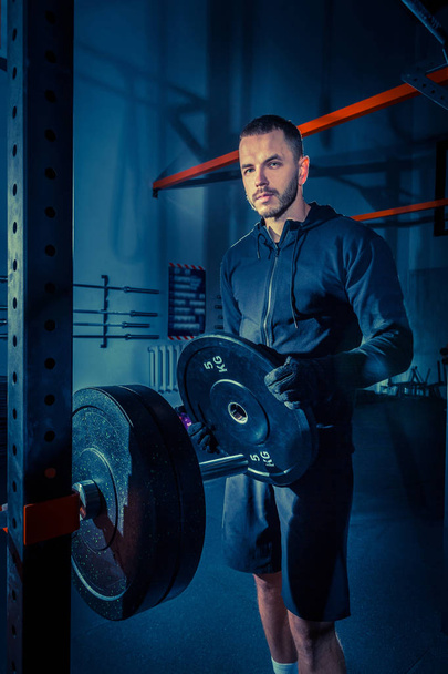 Porträt eines superfitten, muskulösen jungen Mannes, der im Fitnessstudio mit der Langhantel trainiert - Foto, Bild