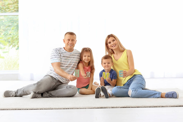 Happy family with word HOME sitting on floor in new apartment - Фото, зображення
