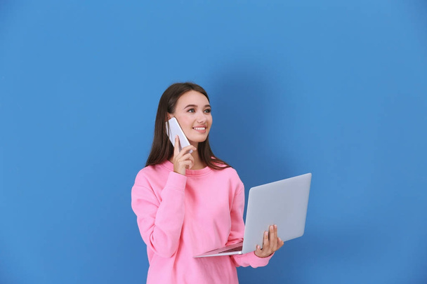 Young lady with laptop talking by phone against color wall - Photo, image