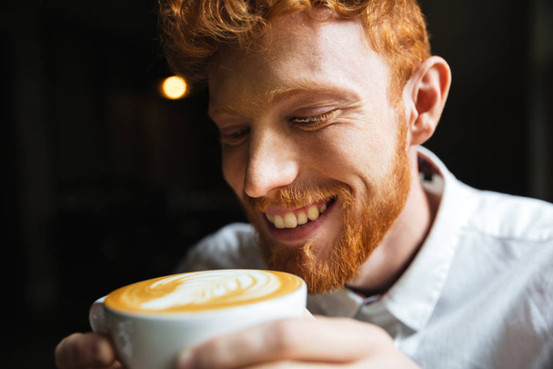 Close-up portrait of smiling curly readhead bearded man tasting  - Фото, зображення