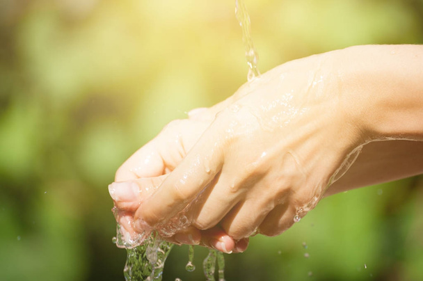 Woman washing hand outdoors. Natural drinking water in the palm. Young hands with water splash, selective focus. Instagram yellow toned - Photo, Image