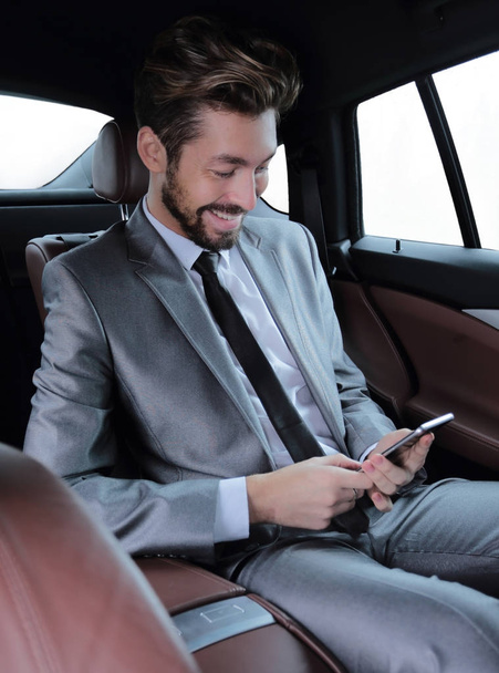man in suit sitting in car and reading messages on smartphone - Fotó, kép