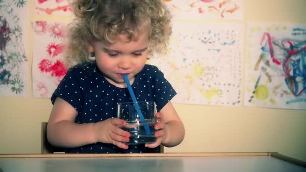 Маленька мила дитина дме повітря через соломинку у склянку з водою
 - Кадри, відео