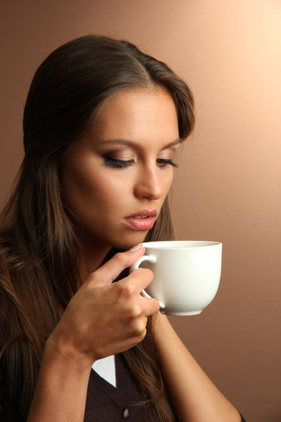 beautiful young woman with cup of coffee, on brown background - Photo, Image