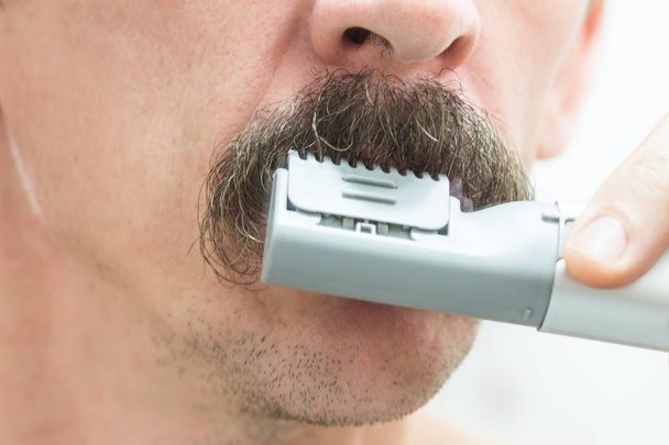 Um homem está a moldar o bigode com um aparador. Close-up
. - Foto, Imagem