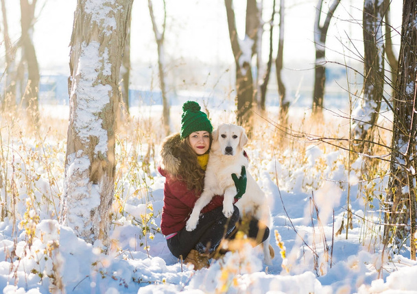 Mooie jongedame knuffelen golden retriever hond in winter forest - Foto, afbeelding