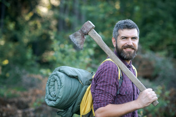Hipster lumberjack with beard and smile hold backpack and axe - Valokuva, kuva