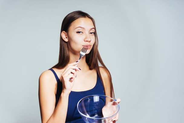 a young beautiful girl in a blue top wants to lose weight, holds an empty glass plate and a fork - Zdjęcie, obraz