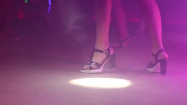 Meisje met mooie benen op hakken close-up dansen in een discotheek met fel licht en rook. - Video