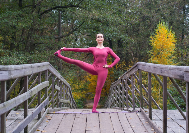 junge Frau steht im Herbst in Yoga-Haltung auf Holzbrücke - Foto, Bild