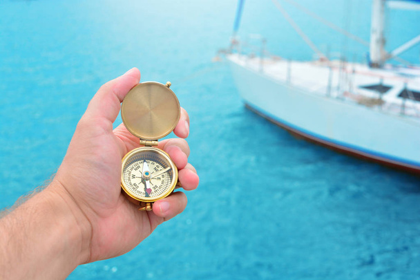 A man's hand with a compass and a yacht in the background - Фото, изображение