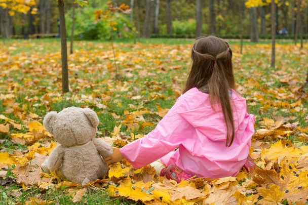 A little girl in a pink raincoat is holding a teddy bear behind her paw - Photo, Image