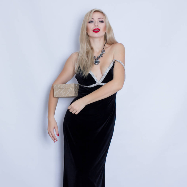 Beautiful elegant young blonde woman in black evening dress holding gift box - Foto, afbeelding