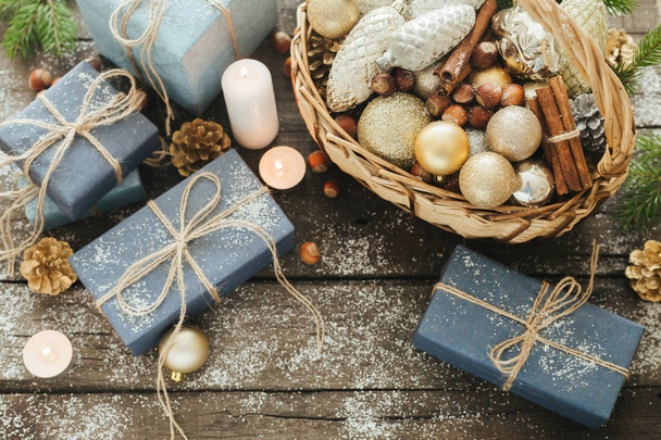 Festive Gifts with Boxes, Candle, Snow, Coniferous, Basket, Cinnamon, Pine Cones, Nuts on Wooden Background. - Photo, Image