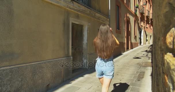 Молодая туристка идет по маленькой улице в солнечный день. Девушка проводит отпуск в Европе, исследуя средневековый старый город
. - Кадры, видео