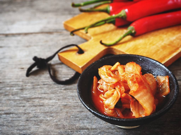 Bowl of traditional korean Kimchi with chilli peppers on wooden background - Foto, Imagem