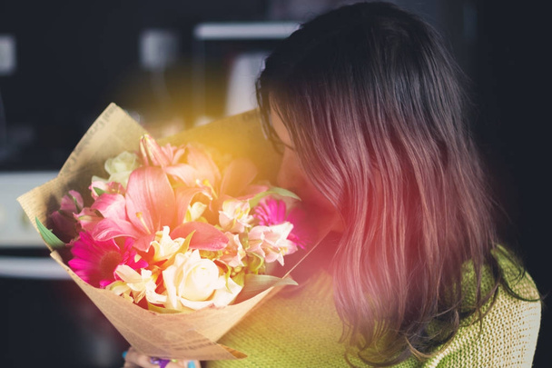 Beautiful girl with dark hair with a bouquet of flowers from a lily, gerbera, white roses and alstroemeria on a dark background. A holiday, a gift. - Photo, image