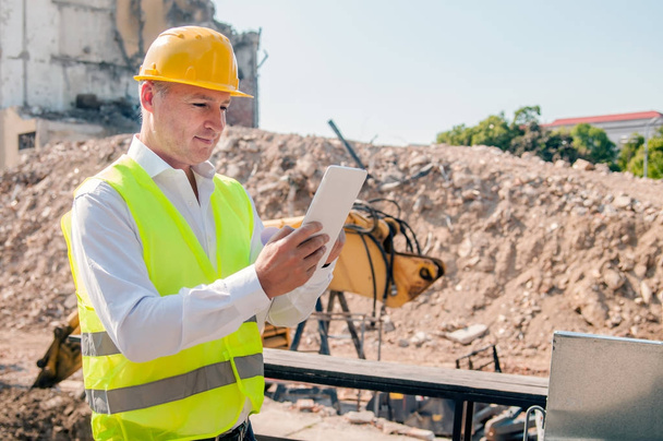 portrait of civil engineer in yellow hardhat using digital tablet at construction site - Foto, afbeelding
