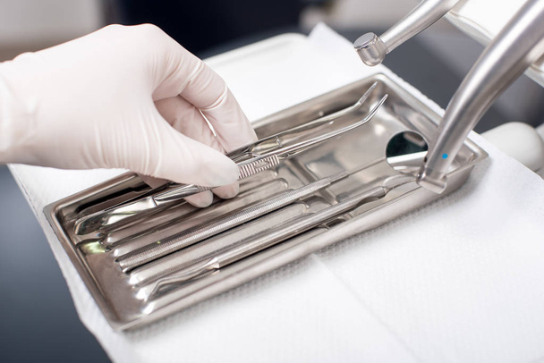 Tandarts met gehandschoende hand is het oppakken van tandheelkundige apparatuur in tandheelkundige kantoor. Close-up - Foto, afbeelding