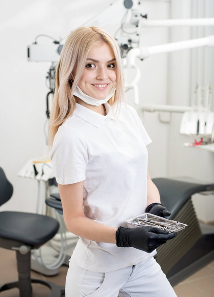 Portrait of young attractive female dentist holding dental instruments at the morden dental office. Doctor wearing mask, black gloves and looking to the camera. Dentistry - Foto, immagini