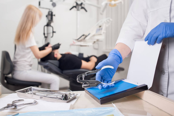 Крупный план рук ассистента в синих перчатках, работающих с зубными инструментами, на размытом фоне стоматолог лечит пациента в стоматологической клинике. Стоматология
 - Фото, изображение