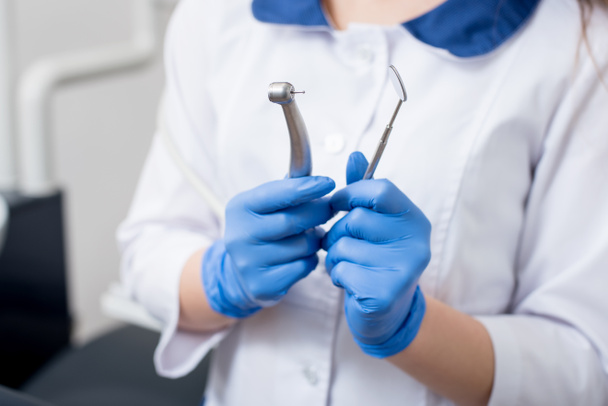 Dentist with blue gloves holding dental equipment at the dental office. Close-up, selective focus on tools. Dentistry - Zdjęcie, obraz