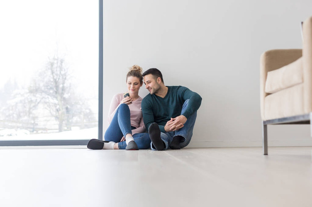 young couple sitting on the floor near window at home - Foto, afbeelding