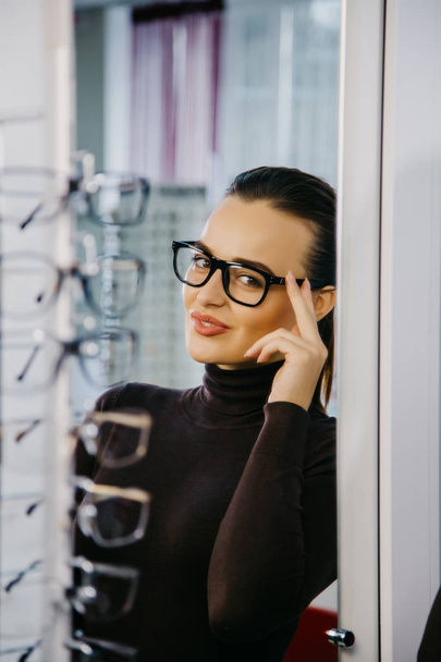 Woman with Eyeglasses in Optical Store - Beautiful girl wearing glasses in optician shop. Ophthalmology. - Фото, изображение