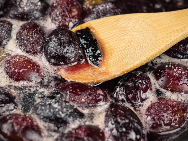 Ripe plums are cooked in sugar syrup and mix with a wooden spoon. - Foto, Bild