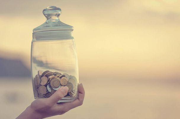 Investitionen, Rente, Steuern und passive Einkommenskonzepte. Münzen in einem Glas in der Hand, den Fokus verschwimmen lassen. Instagram-Foto abgeschwächt - Foto, Bild
