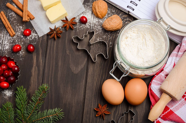 Christmas baking ingredients - cookies cutters, spices, butter, eggs and flour on dark wooden background - Photo, Image