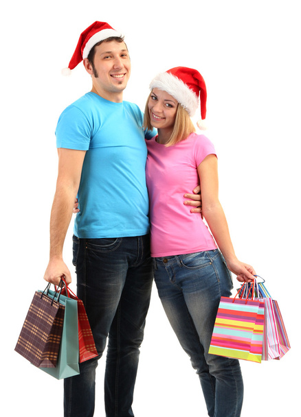 Young couple in Santa hats shopping and holding many shopping bags isolated on white - Fotó, kép