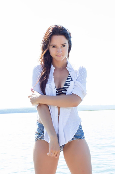 Girl on the beach in a white shirt and short denim shorts - Foto, imagen