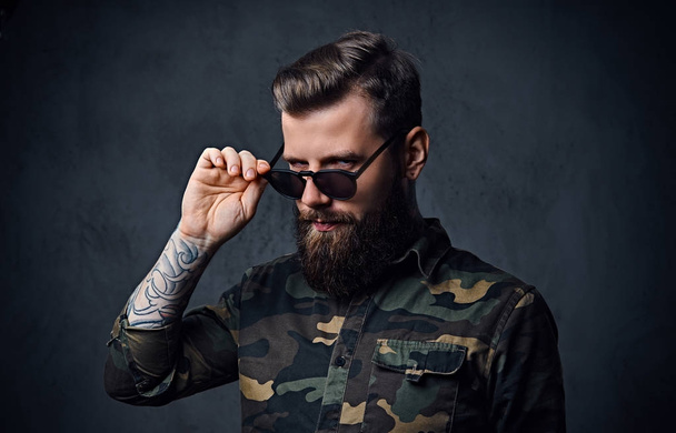 Портрет бородатого татуированного хипстера мужского пола, одетого в военное
 - Фото, изображение