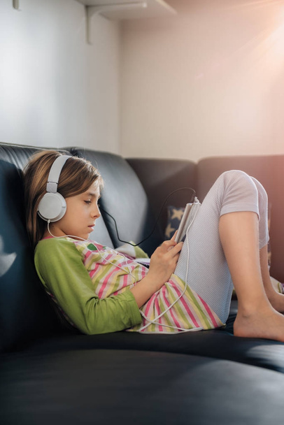 Дівчина сидить на чорному дивані за допомогою планшета і слухає музику
 - Фото, зображення