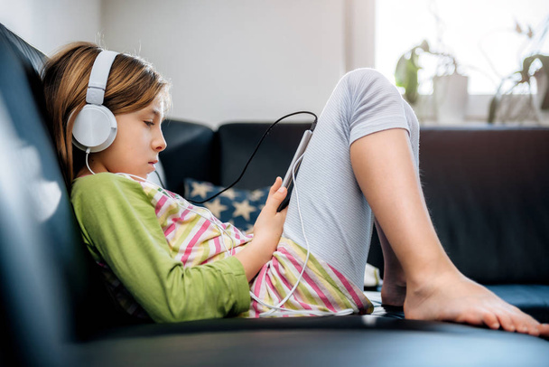 Girl sitting on black sofa using tablet and listening music - Foto, afbeelding
